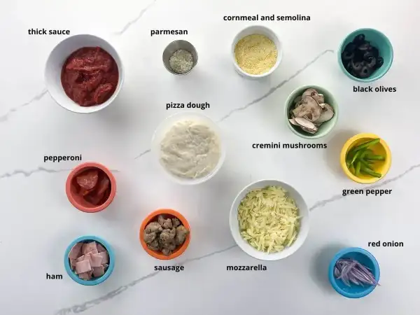 Składniki na pizzę: sos, ciasto, ser, pepperoni, szynka, kiełbasa, pieczarki, oliwki, papryka, cebula, parmezan, mąka kukurydziana.