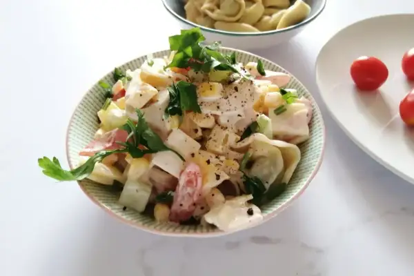 Pyszna sałatka z tortellini, jajka, kukurydzy i pomidorów, udekorowana natką pietruszki.