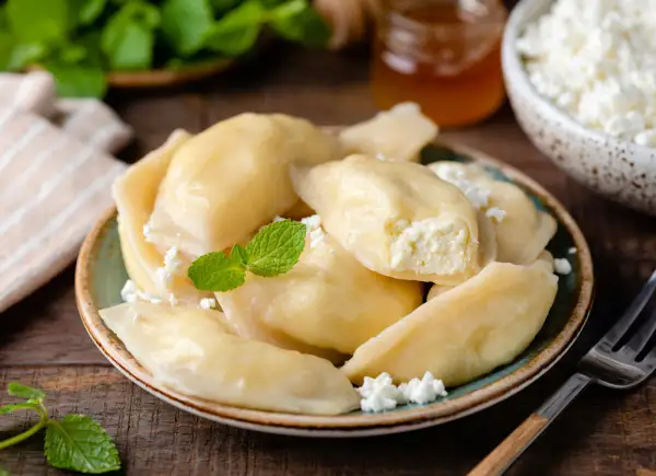 Pyszne pierogi z serem, udekorowane miętą i posypane twarogiem, kuszą swoim domowym wyglądem.